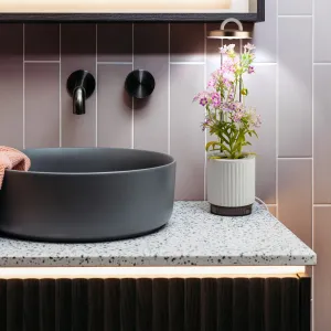 Click & Grow hydroVase, selbstbewässernde Vase mit LED-Beleuchtung, dargestellt mit einer blühenden Pflanze in Innenräumen.