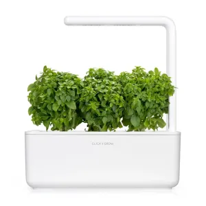 Jardín inteligente Click & Grow con exuberantes plantas de albahaca creciendo bajo el brazo de luz blanca