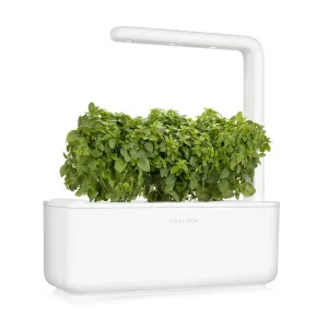 Huerto de hierbas de interior Click & Grow con tres plantas de albahaca enana creciendo bajo un brazo de luz curvo