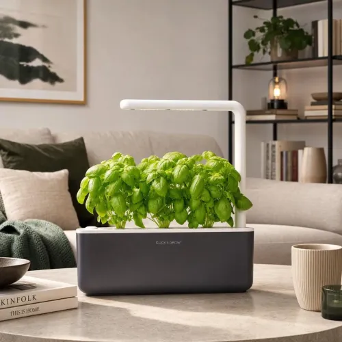Click & Grow Smart Garden 3 indoor herb garden with LED light and leafy greens on a living room table